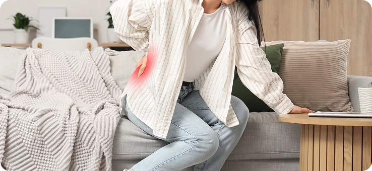 Person sitting on a sofa holding their lower back in pain