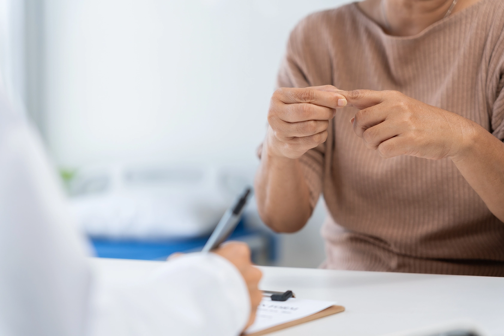 Patient pointing at her finger, explaining joint pain to a doctor during a medical consultation.